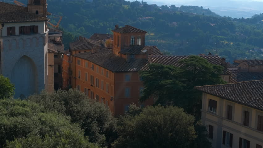 Italian town rooftops landscape with changing shadows. Majestic view of a historic italian town with its characteristic terracotta rooftops, ancient bell tower, and lush green hills