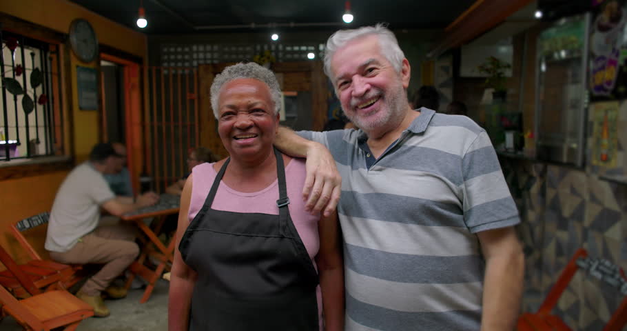 Elderly African American café worker posing with business partner communicating warmth reliability long term collaboration shared history neighborhood connection daily work