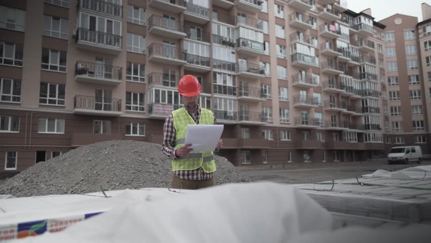 An innovative supervisor in construction in helmet and wearer checks materials and checks quantity against the documents at the construction site of a residential building. Building inspector at work.