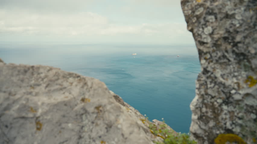 Framed view through limestone rocks on the Rock of Gibraltar overlooking the Strait of Gibraltar with distant cargo ships at sea.