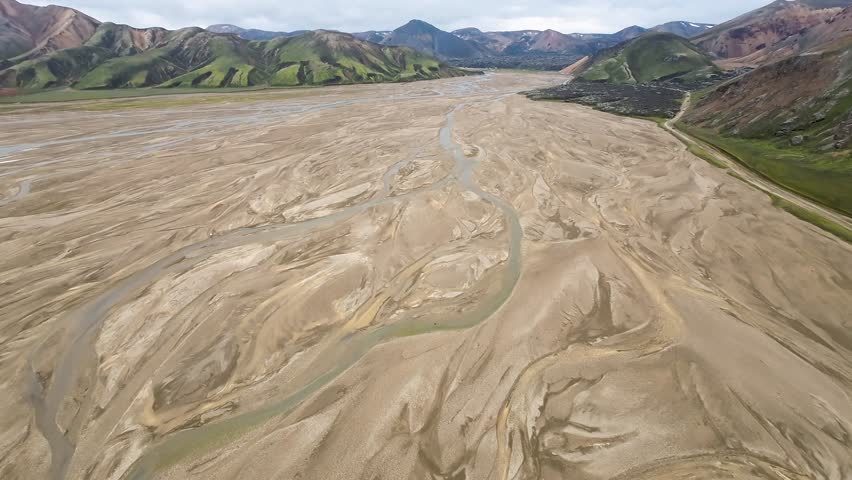 Aerial panoramic view of the colorful rhyolite mountains, volcanic landscape and lake in Landmannalaugar, Iceland. Dramatic highland scenery with green hills, lava fields and winding road in the Icelandic Highlands, popular destination for hiking and adventure travel.