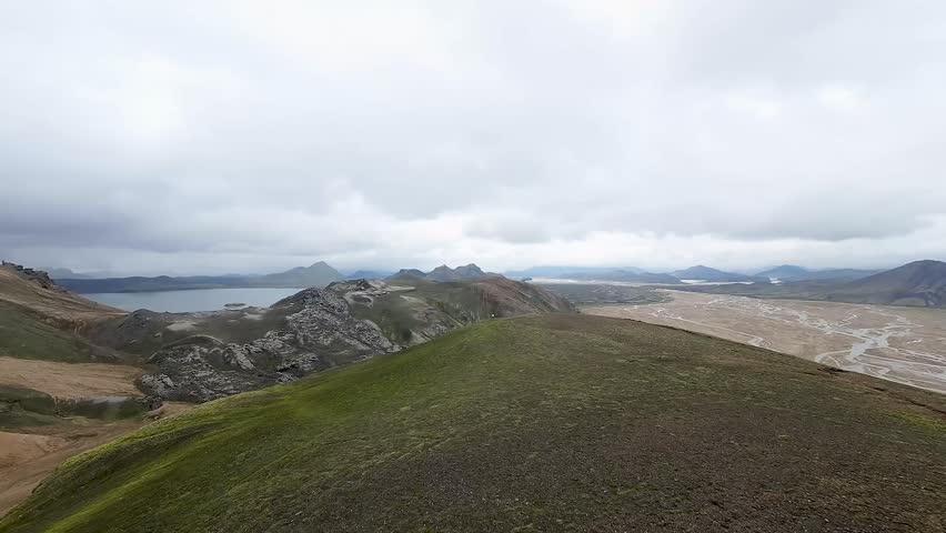 Aerial panoramic view of the colorful rhyolite mountains, volcanic landscape and lake in Landmannalaugar, Iceland. Dramatic highland scenery with green hills, lava fields and winding road in the Icelandic Highlands, popular destination for hiking and adventure travel.