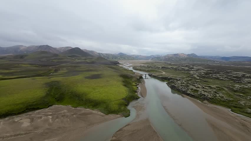 Aerial panoramic view of the colorful rhyolite mountains, volcanic landscape and lake in Landmannalaugar, Iceland. Dramatic highland scenery with green hills, lava fields and winding road in the Icelandic Highlands, popular destination for hiking and adventure travel.
