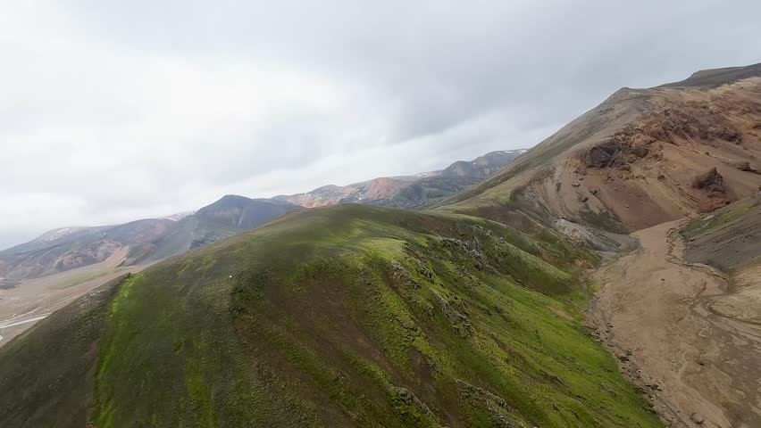 Aerial panoramic view of the colorful rhyolite mountains, volcanic landscape and lake in Landmannalaugar, Iceland. Dramatic highland scenery with green hills, lava fields and winding road in the Icelandic Highlands, popular destination for hiking and adventure travel.