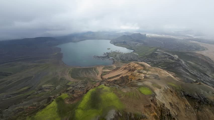 Aerial panoramic view of the colorful rhyolite mountains, volcanic landscape and lake in Landmannalaugar, Iceland. Dramatic highland scenery with green hills, lava fields and winding road in the Icelandic Highlands, popular destination for hiking and adventure travel.