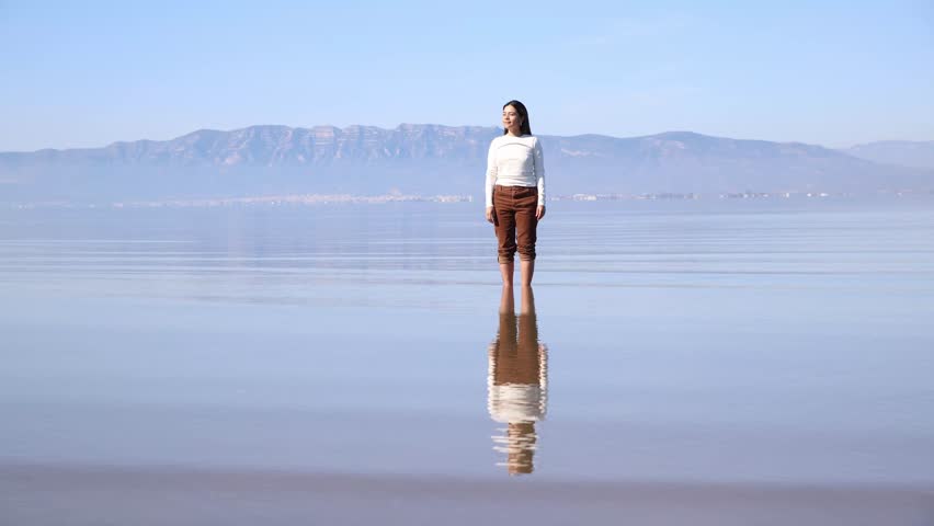 A young woman standing still in shallow water, moving gently to convey a sense of inner peace and mindfulness