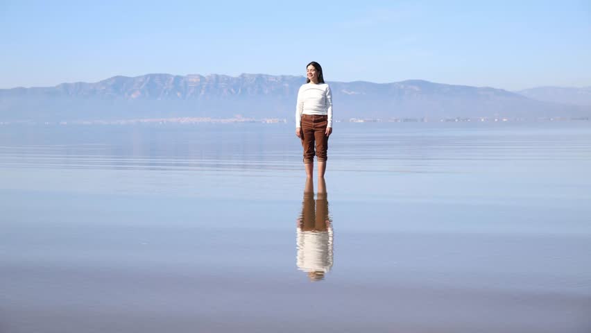 A young woman standing still in shallow water, moving gently to convey a sense of inner peace and mindfulness