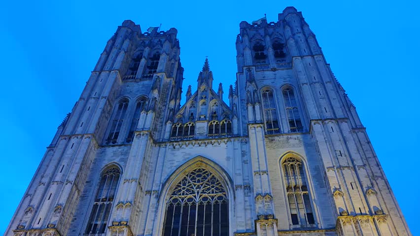 Majestic Gothic facade of the Cathedral of St. Michael and St. Gudula in Brussels at dusk with twin towers and ornate stone carvings under a blue evening sky.