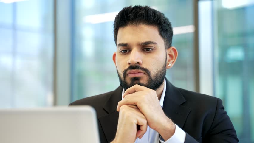 Businessman thinking about problem solving while working on laptop sitting at workplace in business office. Thoughtful serious manager in formal suit is busy with startup project on computer. Close up