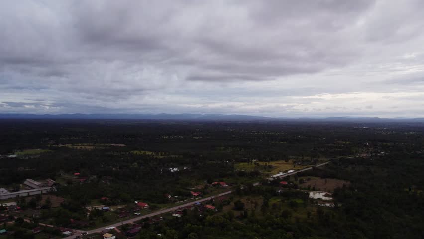 Forward motion flying view of evening hour rural tropical landscape with sporatic building along the land and cloudy overcast sky.