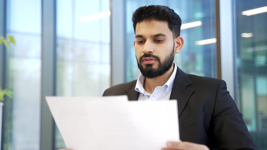 Serious businessman reviewing financial documents while sitting in modern business office. Thoughtful executive checking analyzing reports, contracts, investment data or corporate accounting papers. 