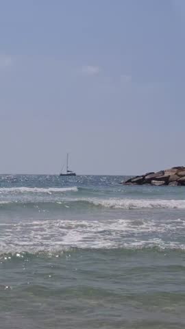 Beautiful view of Ashdod beach in Israel with sea waves, stone breakwater, and a sailboat on the horizon.