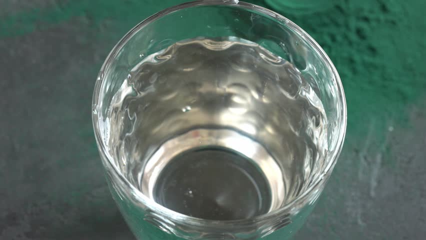 Pouring green spirulina algae powder into a glass of water. Nutritional supplement.
