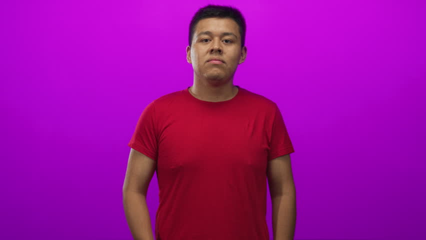 Young man smiling and reaching out with open hand and palm visible in studio against magenta backdrop; inviting.