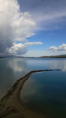 Cloudy Beach Scene. Tranquil Shoreline Beneath Turbulent Sky Reflecting Softly On Water Surface