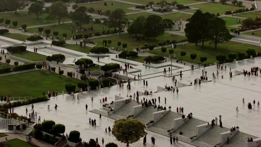 Aerial footage of the Mazar-e-Quaid, the mausoleum of Muhammad Ali Jinnah, located in Karachi, Pakistan. The striking white marble structure features a large dome and arched entrances, surrounded by landscaped gardens and a spacious courtyard. Numerous visitors walk around the site, reflecting its importance as a national monument and popular tourist destination. This shot highlights the architectural beauty, cultural heritage, and solemnity of Pakistan’s most iconic landmark.