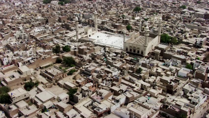Aerial footage of Jamia Masjid Al-Sadiq, a grand mosque located in Bahawalpur, Punjab, Pakistan. The mosque features multiple domes, tall minarets, and a spacious courtyard where people gather. Surrounded by densely packed urban buildings, the mosque stands out as a focal point of the community, showcasing Islamic architecture, cultural heritage, and the significance of religious spaces in traditional city life.