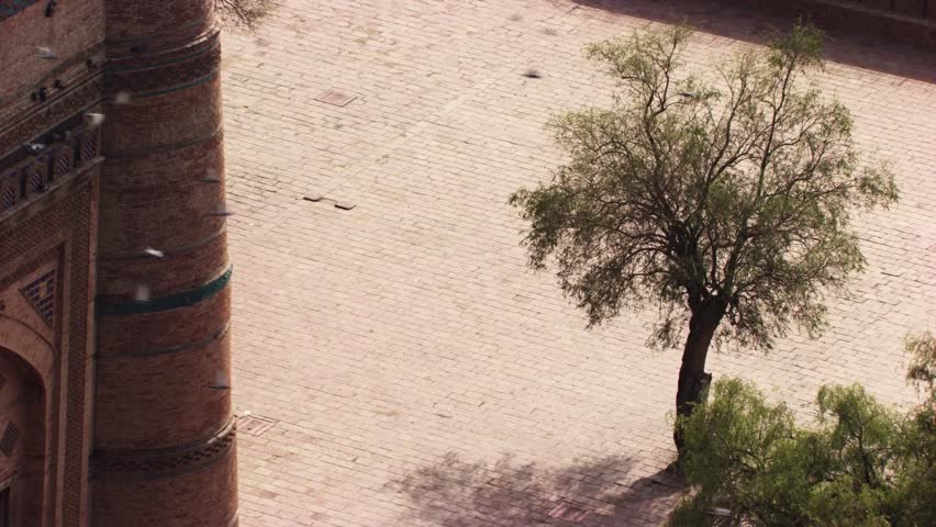 Aerial footage of the Tomb of Shah Rukn-e-Alam, a historic landmark in Multan, Pakistan. The octagonal red-brick structure is adorned with intricate blue tile work and crowned with a large white dome surrounded by smaller decorative domes. The tomb is set within a spacious courtyard with green lawns, pathways, and gateway structures, where visitors walk and gather. This shot highlights Islamic architecture, cultural heritage, and the historical significance of one of Pakistan’s most iconic monuments.