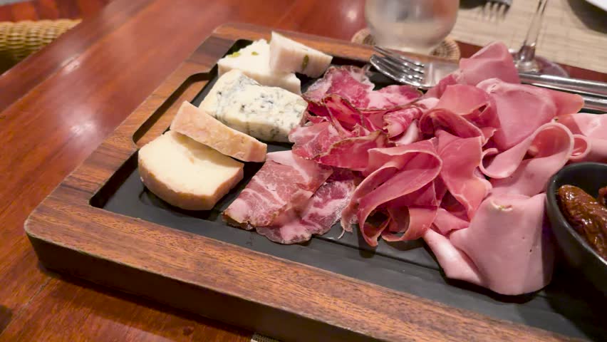 Close-up panning shot of a wooden platter with prosciutto, salami, mortadella, and blue cheese