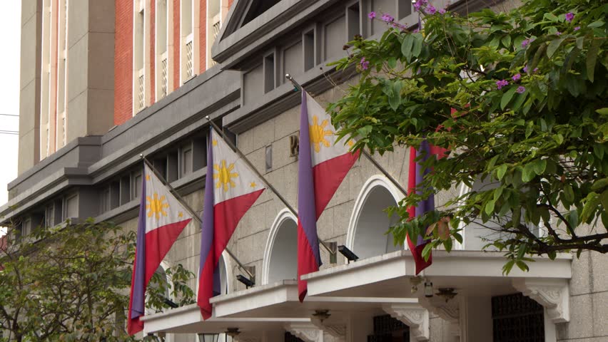 A low angle shot tilts up toward colonial architecture and waving national flags in Manila