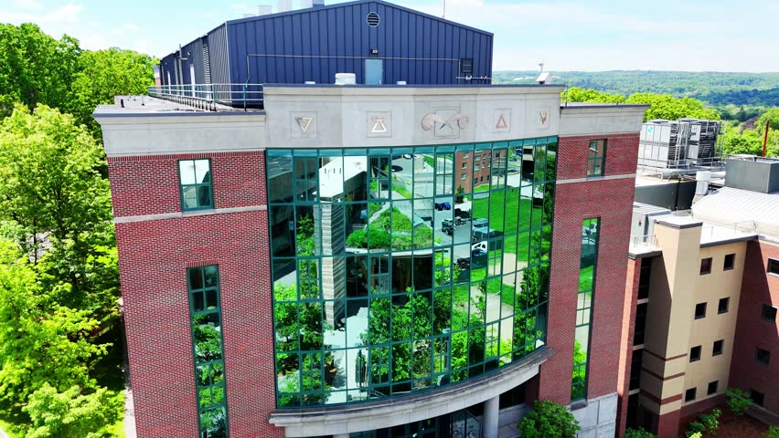 The wind forces the leaves below to shutter against each other as people exit from a place that conducts scientific experiments, opportunities to learn, and educational and industry advancement in fields of STEM. Syracuse, NY, USA - May 30, 2025.