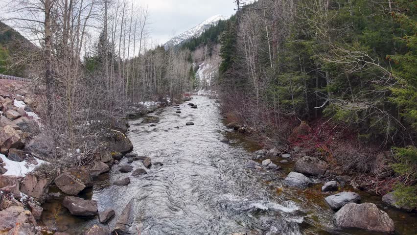 Aerial drone view of rocky river channel winding through forested valley in Montana with flowing water and bare trees.
