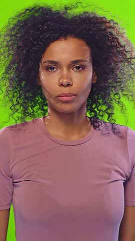 Curly haired African American woman showing frustration and covering ears with hands in front of green background in emotional expressions. Stress, emotion, noise, discomfort concept
