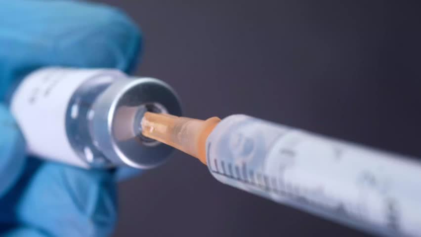 Gloved hand drawing covid-19 vaccine from glass vial into syringe close-up