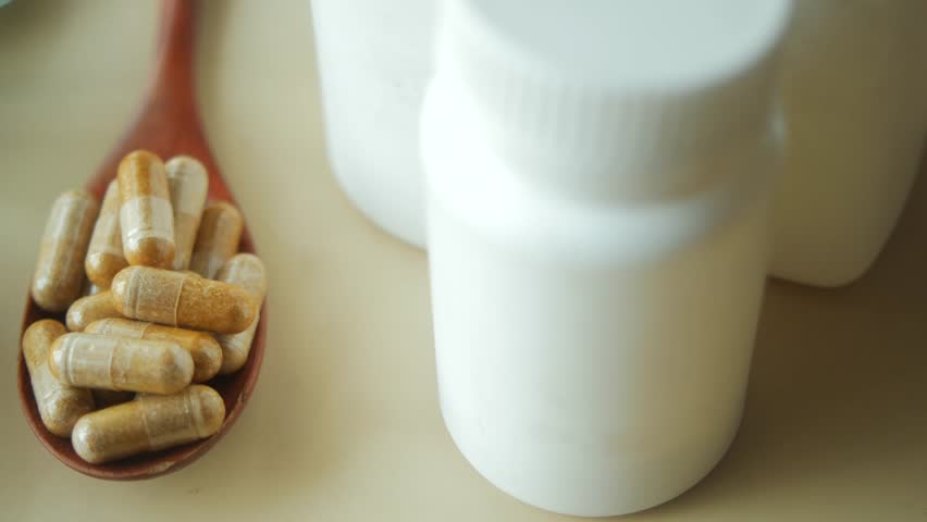 Close up on wooden spoon filled with herbal capsules next to white pill bottles