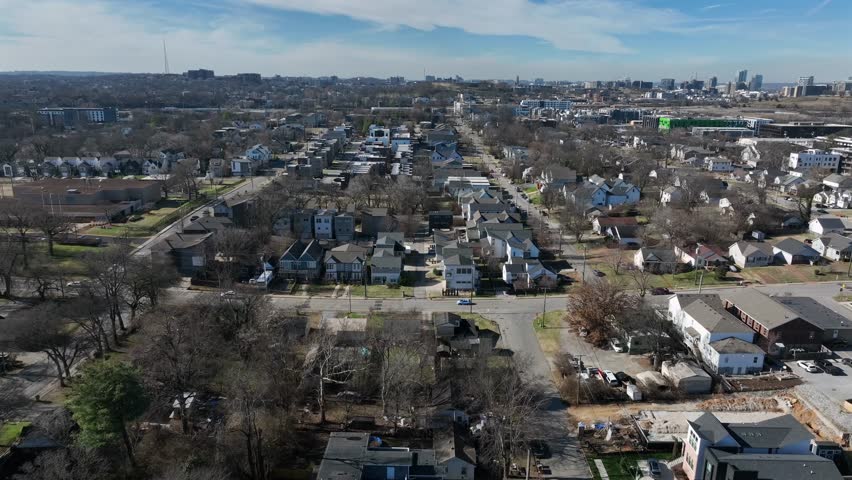 Aerial winter view of Nashville residential neighborhood with rows of single-family homes, suburban streets and downtown skyline visible in distance under clear daylight. Sunlight in January.