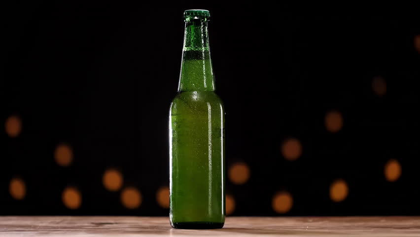 Cold green refrigerated wheat or lager beer bottle, condensation droplets cover surface of container, highlighting refreshing and crisp quality isolated on black background