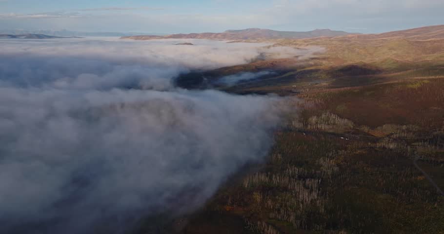 Aerial establishing dolly of campers in forested clearing near Grand Lake Colorado, fog encroaches with cloud shadows on trees