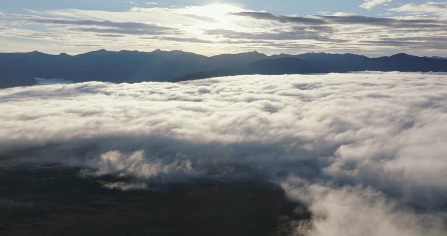 Aerial sunrise over fog covering Grand Lake near Rocky Mountain National Park, drone panoramic dolly to sunlight across clouds
