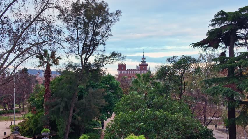 Slow panning shot inside Parc de la Ciutadella showing lush trees, birds in flight and historic architecture in Barcelona, Spain.
