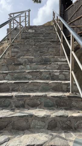 First person view of man or woman walking up stone staircase with metal railings, scenic outdoor path. POV of climbing natural stone steps on walking trail, travel, hiking and active lifestyle concept