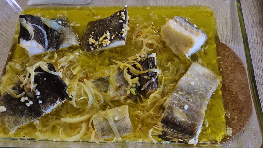 Homemade Portuguese cod with onions simmered in golden olive oil, close-up in a glass baking dish showing juicy fish chunks, caramelized onion rings and rustic family style comfort food.