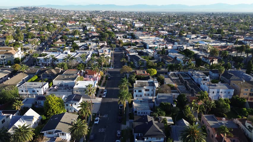 Neighborhood north of Bluff Park, Coronado Ave extends distant hills with dense residential blocks, consistent street alignment. Mixed roof, scattered palms, hazy mountain backdrop, Long Beach, CA. US
