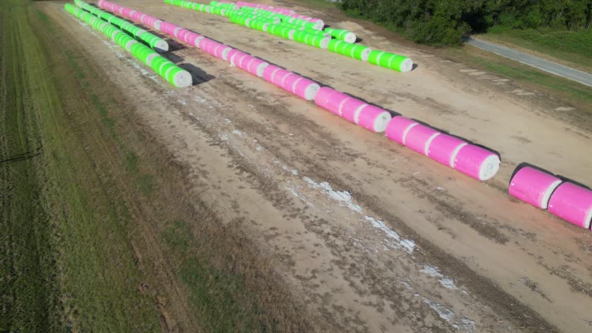 Plastic wrapped upland cotton (Gossypium hirsutum) modules organized in long parallel rows across agricultural land near Headland in Henry County, Alabama, aerial push in shot.