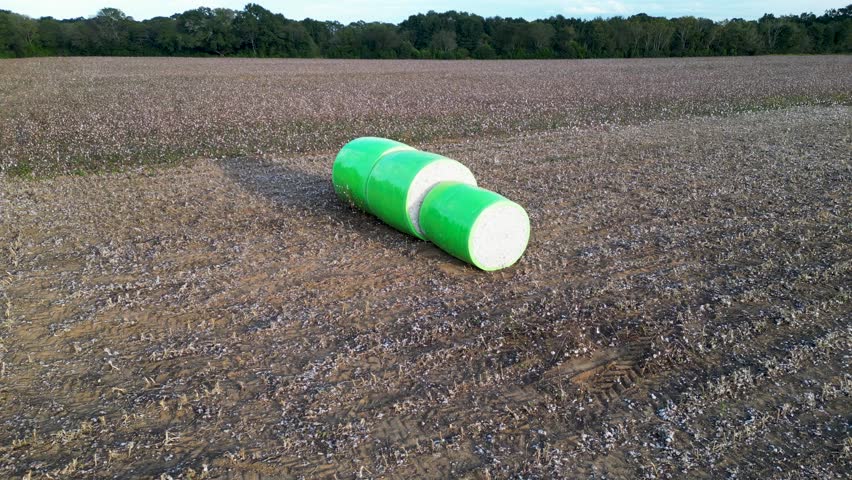 Single wrapped cotton bale positioned beside harvested cotton field near Headland, Henry County, Alabama, United States during autumn harvest season, aerial view.