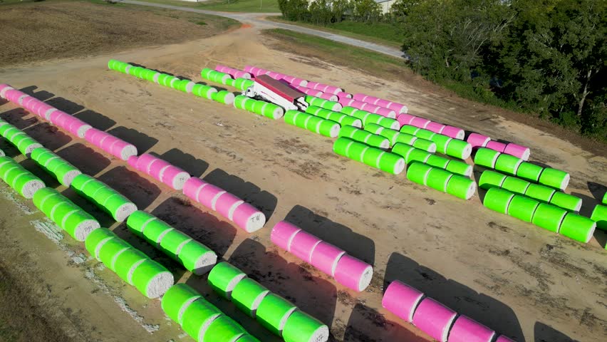 Plastic wrapped cotton modules arranged in long parallel rows across farmland near Headland in Henry County, Alabama within the Wiregrass agricultural region while transport truck collects bales