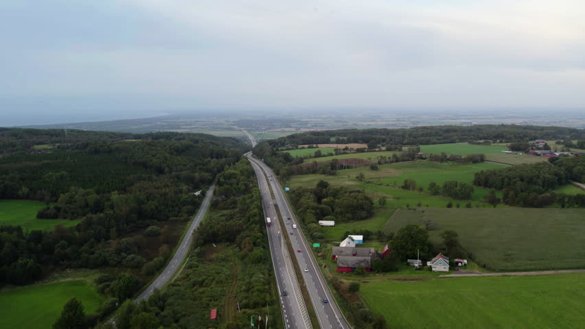 Drone view of highway traffic crossing forests and farmland at Hallandsåsen ridge in Sweden. Scenic Scandinavian countryside landscape with rural homes and transport infrastructure.