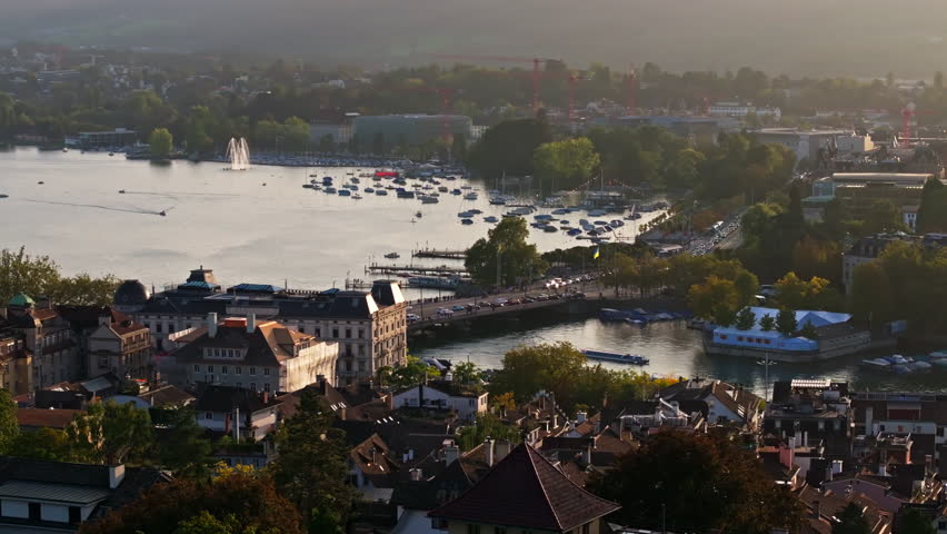 Smooth circular drone shot orbiting the Quaibrücke in Zurich with sweeping views over Lake Zurich and the city waterfront. Golden light, calm water reflections, and cinematic Swiss urban atmosphere.