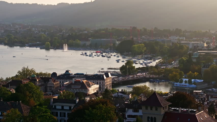 Aerial drone shot from Kunsthaus Zürich looking toward Lake Zurich with sweeping views over the Quaibrücke and city waterfront. Golden light, calm water, and cinematic Swiss urban atmosphere.