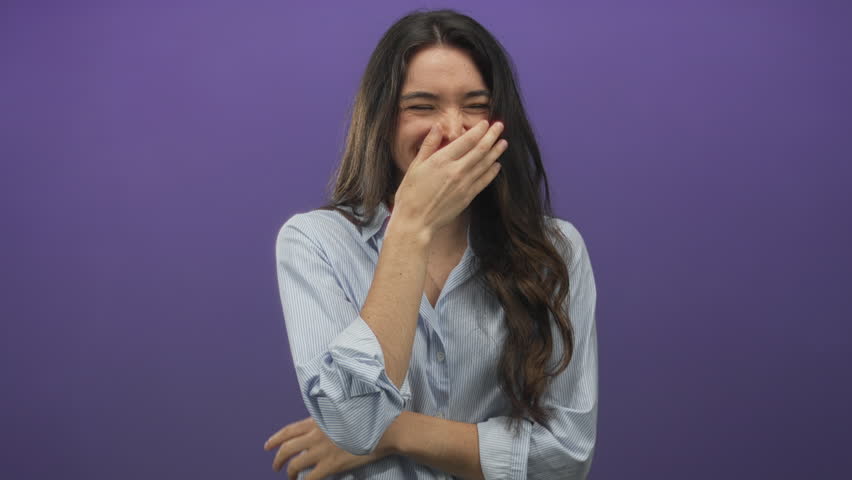 Woman wearing striped shirt covering mouth with hand and crossing arms in purple studio setting; joy.