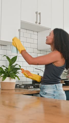 Smiling Young Black Woman with Natural Hair Thoroughly Cleaning Modern Kitchen Cabinets