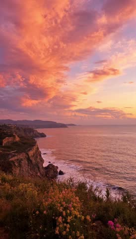 Breathtaking sunset over the rugged ocean cliffs with vibrant orange clouds and crashing waves at dusk