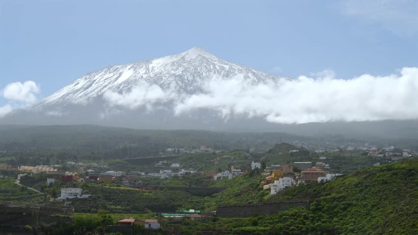 Majestic view of the snow capped Teide volcano on the island of Tenerife. Fluffy white clouds drift across the peak and the blue sky