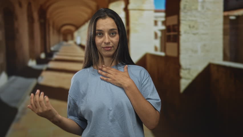 Woman placing hand on chest on old town street, looking toward camera with a gentle expression; contemplation.