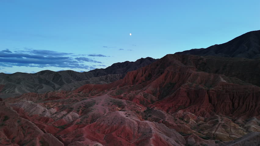 Red canyon ridges at dusk with moon