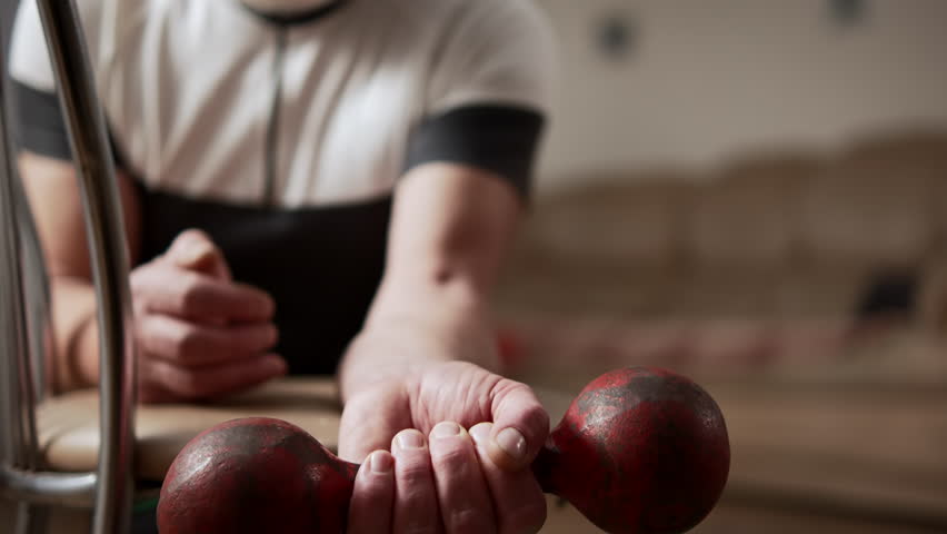 Elderly man performs an exercise with dumbbell in his hand, training his forearm